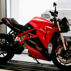 Motocicleta roja y negra Energica RS, lista para la acción. Detrás, un coche blanco.