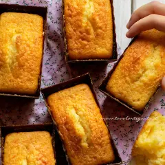 Plumcake yogurt dorati e soffici, pronti per essere gustati. Una mano ne afferra uno, mentre un pezzetto mostra la morbidezza interna.