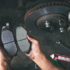Ręce mechanika porównują zużyte i nowe klocki hamulcowe. Czas na wymianę klocków hamulcowych w samochodzie.