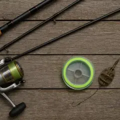 Wędka, kołowrotek, żyłka, haczyk i podajnik do metody feeder na drewnianym tle.