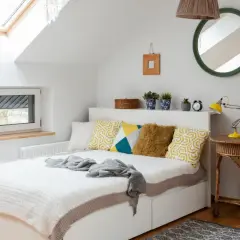 Chambre sous pente lumineuse avec lit blanc, coussins géométriques, et un puits de lumière. Une belle idée peinture pour un espace cosy.