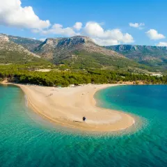 Una spiaggia a forma di lingua di sabbia dorata si estende nel mare turchese della costa croata, con montagne verdi sullo sfondo.