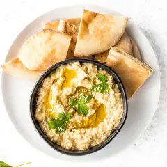 Un bol de caviar d'aubergine crémeux, garni d'huile d'olive, de persil et de sésame, servi avec des morceaux de pain pita.