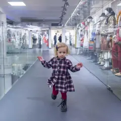 Mała dziewczynka biega po muzeum dla dzieci im. Janusza Korczaka, mijając gabloty z tradycyjnymi strojami.