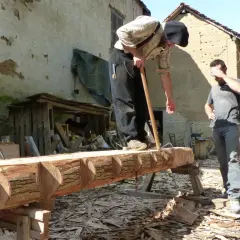 Deux hommes travaillent sur un tronc d'arbre, pratiquant l'équarrissage bois avec une hache. Le bois est façonné avec soin.