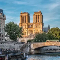 Katedra Notre Dame w Paryżu nad Sekwaną, z łodzią turystyczną i mostem w tle.