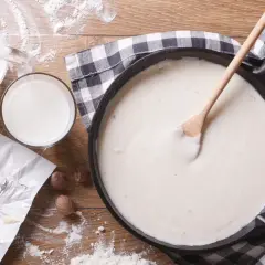 Kremowy sos beszamelowy do lasagne w patelni, obok mleko, masło i gałka muszkatołowa.