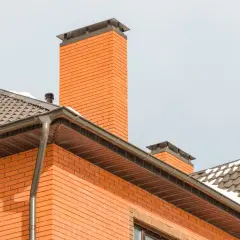 Ceglany komin i dach domu. Zastanawiasz się, ile kosztuje wybudowanie komina?