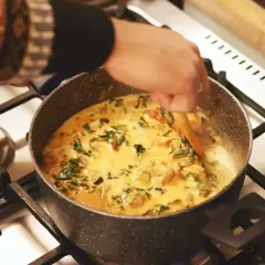 Ręka miesza kremowe curry z zielonymi warzywami w garnku. Idealny garam masala przepis na aromatyczne danie.