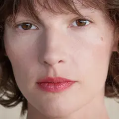 Zbliżenie na twarz kobiety z brązowymi oczami i falowanymi włosami. Retinol dla kogo? Dla każdej kobiety pragnącej odmłodzonej skóry.