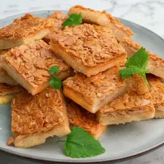 En hög med fyrkantiga bitar av en härlig mandelkaka, perfekt för ett "baka i långpanna deluxe recept". Garnerad med mynta.