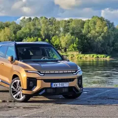 Złoty KGM Actyon SUV stoi nad rzeką, otoczony zielenią.