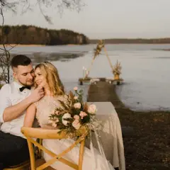Młoda para siedzi blisko siebie nad jeziorem, tworząc intymną chwilę. Tylko my dwoje, w otoczeniu natury, celebrujemy miłość.