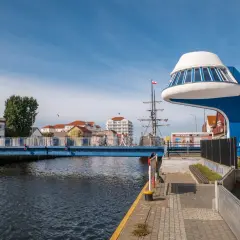 Niebieski most nad Regą w malowniczym mieście. W tle żaglowiec i nowoczesna architektura.