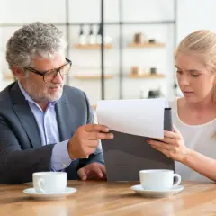 Hombre y mujer revisan documentos. Él explica que un precontrato es vinculante. Tazas de café en la mesa.