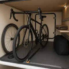 Comment fixer vélo dans soute camping car : un vélo noir est attaché au sol avec des sangles dans la soute d'un camping-car. Une roue est détachée.