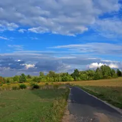 Droga wijąca się przez malownicze **wzniesienia łódzkie**, otoczona zielenią i błękitnym niebem z chmurami.