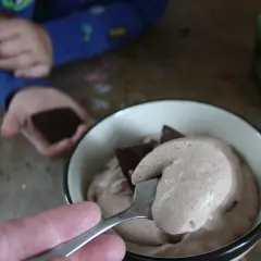 En sked med krämig after eight mousse lyfts ur en skål. En barnhand håller en chokladbit i bakgrunden.