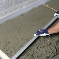 Ręce w rękawiczkach wyrównują świeżą wylewkę za pomocą łaty.