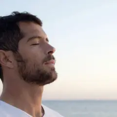 Un homme au profil serein, yeux clos, savoure l'air marin. Sa barbe de 3 jours, d'environ 3 mm, accentue son charme naturel.