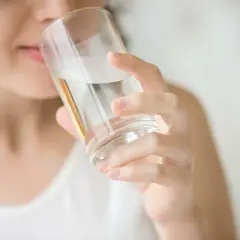 Kobieta pije wodę z filtra, która ma gorzki smak.