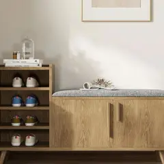 Stylish entryway decor ideas: a wooden shoe cabinet with a padded bench top, open shelves with shoes, and a decorative plant.
