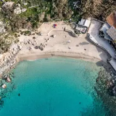Widok z lotu ptaka na rajską zatokę na Malcie, z turkusową wodą, piaszczystą plażą i budynkami przy brzegu.