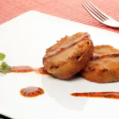Dos manitas de cerdo rebozadas y fritas, servidas con salsa roja y perejil en un plato blanco.