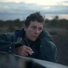 Skådespelare Frances McDormand lutar sig mot en bil i ökenlandskap, med en cigarett i handen.