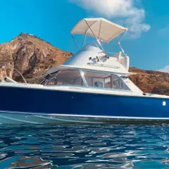 Barca blu e bianca con tendalino, in rada con sfondo montuoso. Un esempio dei tipi di barche top 7 per un'estate indimenticabile.