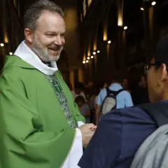 Uśmiechnięty ksiądz w zielonej szacie wita młodego mężczyznę. Warto wiedzieć, jak się zwracać do biskupa, ale i do każdego kapłana z szacunkiem.