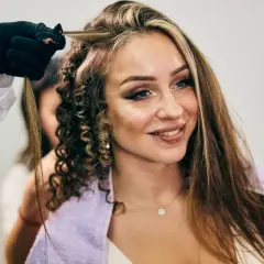 Stylist tworzy loki na włosach kobiety z widocznymi chunky highlights.