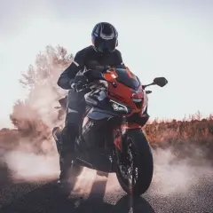 Motocyklista w kasku i kombinezonie na czerwono-czarnym motocyklu Barton Blade 125, unoszący kurz. Czy motocyklem 125 można jeździć po autostradzie?