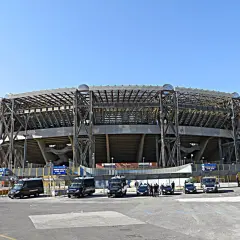 Imponujący stadion w Neapolu, z charakterystyczną konstrukcją i kilkoma samochodami policyjnymi przed wejściem.