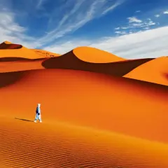 Un voyageur solitaire traverse la majestueuse dune du Sahara sous un ciel bleu éclatant.