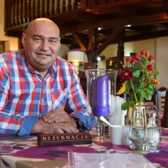 Łysy mężczyzna w kratę siedzi przy stole z kwiatami i świecą.
