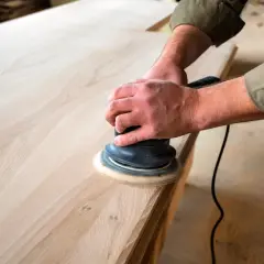 Man lijando madera con una lijadora orbital, preparando una superficie lisa para un proyecto.