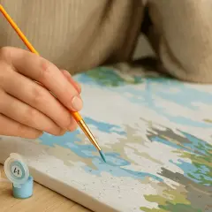 Hand malt mit Pinsel auf Leinwand, daneben kleine Farbtöpfe mit Zahlen.