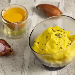 Una ciotola di salsa bernese cremosa, guarnita con erbe aromatiche, accanto a un tuorlo d'uovo e scalogni.