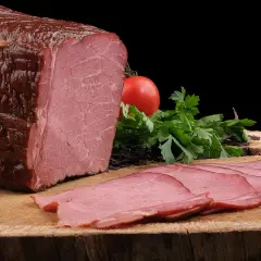 Pyszna, wędzona szynka po peklowaniu, pokrojona w cienkie plastry, z pomidorem i natką pietruszki.