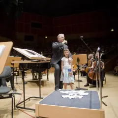 Zbigniew, kompozytor i dyrygent, z córką na scenie przed orkiestrą.