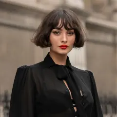 Eine Frau mit einem lässigen, **choppy bob** und rotem Lippenstift trägt eine transparente schwarze Bluse.
