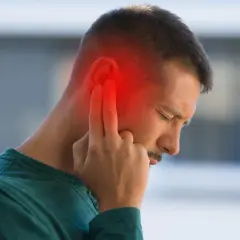 Hombre con dolor de oído, señalando la zona afectada con un halo rojo. Podrían ser sabañones en las orejas.