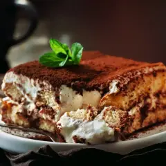 Pyszne tiramisu przepis na talerzu, posypane kakao i udekorowane miętą. Idealne na deser.