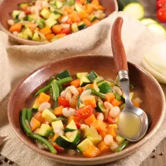 Un plato humeante de menestra de verduras, con judías verdes, zanahoria, calabacín y alubias blancas, servido con una cuchara.