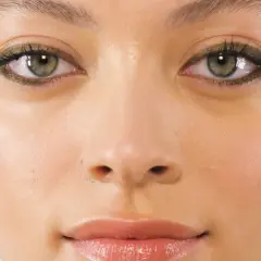 Primo piano di una ragazza con un trucco occhi audace e gioielli dorati. I suoi occhi verdi marroni sono evidenziati da un eyeliner scuro e scintillante.