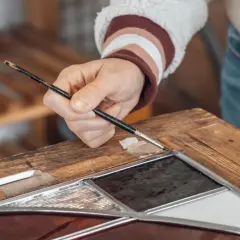 Ręka maluje pędzelkiem detale na drewnianej ramie, która kiedyś stanowiła część **starych drzwi drewnianych zewnętrznych**.