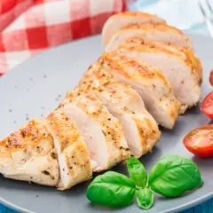 Tranches de blanc de poulet grillé, assaisonné de poivre et d'herbes, servi avec des tomates cerises et du basilic frais.