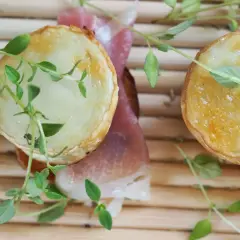 Dos bocaditos con crujiente de queso de cabra fundido y jamón serrano, adornados con hierbas frescas.