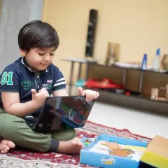 Mały chłopiec, mój syn, uczy się francuskiego przez tablet, siedząc na dywanie.